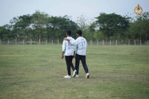 Two male college cricket players in blue jerseys talking animatedly on the field during the Ranbhoomi inter‑college tournament at Brahmastra 2025.