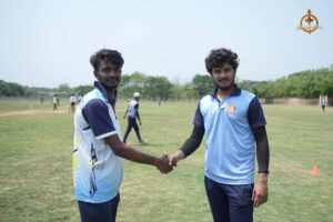 Two college cricket team captains shaking hands on the pitch during the Ranbhoomi (Cricket) event at Brahmastra 2025, with teammates and umpires nearby.