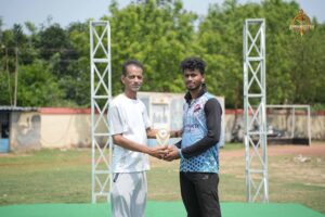 A student cricketer receives a trophy from a faculty member during the award ceremony at Brahmastra 2025.