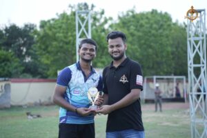 Cricket team captain presenting a trophy to the best player during the Ranbhoomi event at Brahmastra 2025.
