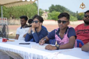Student anchors delivering live cricket commentary during the Ranbhoomi event at Brahmastra 2025, equipped with microphones and match notes.