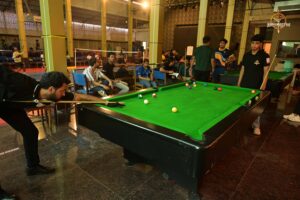 A man playing billiards in a bright room with an audience observing.