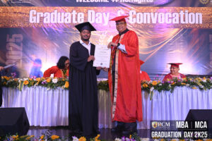 Graduate receives certificate on stage at convocation event with floral decorations.