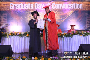 Graduate receives certificate from official on decorated stage during RCM MBA/MCA convocation.