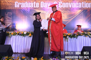 Graduate receives certificate at RCM MBA/MCA Graduation Day 2K25 ceremony, stage with flowers.