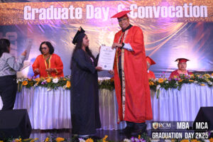 Graduate receives certificate from person in red robe at convocation ceremony with floral decor.