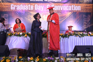 Graduate receiving certificate on stage at 2025 convocation with flowers and signage.