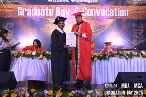 Graduate receives certificate on stage during 2K25 convocation, with floral decorations and banner.