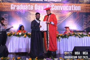 Graduate receiving certificate at a graduation ceremony with floral decor and attendees.