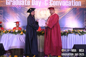 Graduate receives certificate from faculty during ceremony with floral stage decorations.