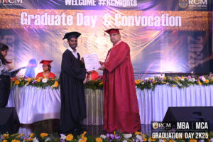 Individual in graduation attire receiving certificate on stage, banner shows "Graduation Day 2K25".
