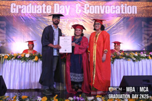 Graduate receiving certificate at RCM MBA and MCA convocation beneath event banner.