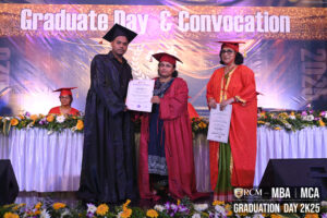 Graduate receiving certificate on convocation stage, flowers and banner in background, 2025.