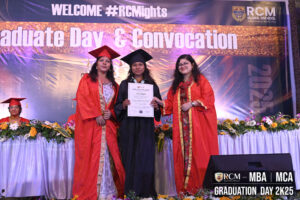 Three individuals in academic regalia at RCM Global B-School graduation ceremony with banner.