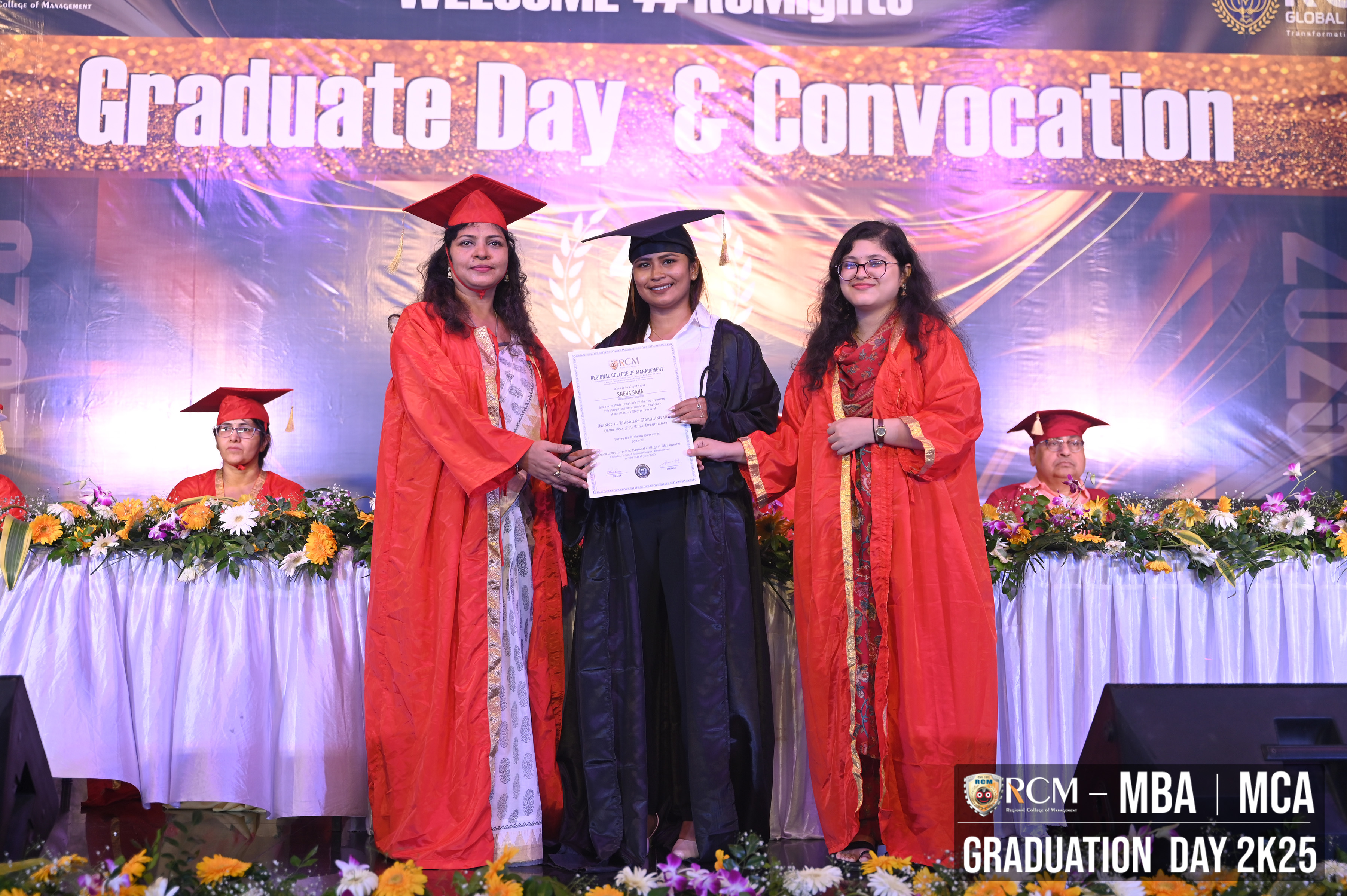 Graduation ceremony with people in academic robes on stage holding a certificate.