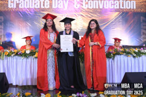 Graduate receives certificate from two individuals in red robes at ceremony with a banner.