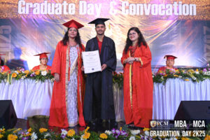 Graduate on stage with certificate, two in red robes beside, "Graduate Day 2K25" backdrop.