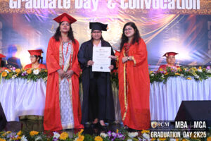 Graduation ceremony with three people on stage holding a certificate, decorated with flowers.