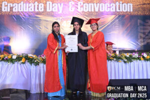 Graduation ceremony on stage with three individuals holding a certificate, floral backdrop.