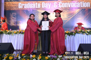 Graduate receives certificate at RCM 2025 convocation, with two in red robes on stage.