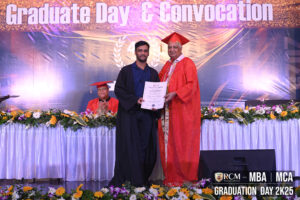 Graduate receives certificate from person in orange robe at event with flowers and "Graduate Day."