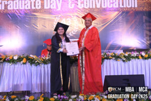 Person in graduation attire receives certificate on decorated stage with "Graduate Day 2K25" backdrop.