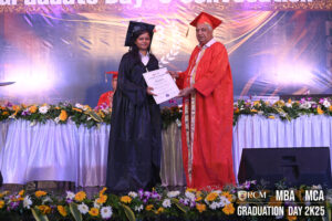 Graduate receiving certificate from faculty, both in academic regalia, at RCM ceremony.