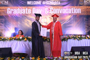 Graduate receiving certificate on stage during convocation, with decorated stage and seated attendee.