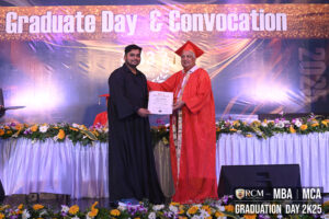 Graduate and faculty on stage, RCM 2K25 event, holding certificate amidst decorations.