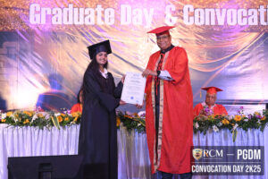 Graduate in black cap and gown receives certificate from faculty in red during convocation.