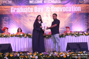 Graduate receiving certificate at Regional College of Management convocation event on decorated stage.