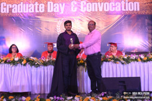 Graduate in black gown receives a trophy on stage during a convocation ceremony.