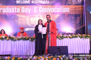 Graduate receives certificate at RCM Global School convocation; decorated stage, seated graduates.