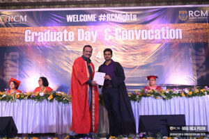Graduation ceremony at RCM, banner reads "Graduate Day & Convocation," individual receiving certificate.