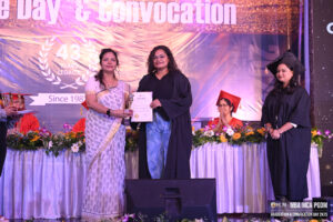 Graduation ceremony with graduates, a certificate presentation, flowers, and event banners.