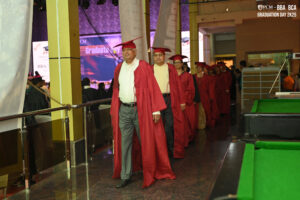 Individuals in red graduation gowns at an indoor ceremony, pool table in foreground.