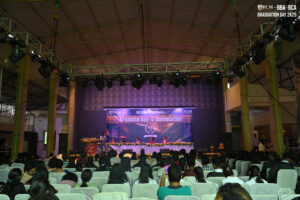 Graduation ceremony 2025 in indoor venue with stage and audience, decorated with banners.