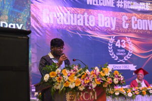 Speaker at podium with flowers, banner reads "Graduate Day & Convocation," 43 years legacy.