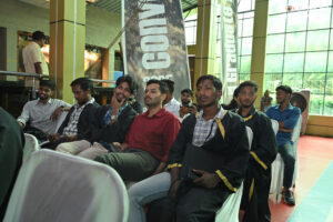 Individuals seated indoors with banners wearing graduation gowns; formal event setting.