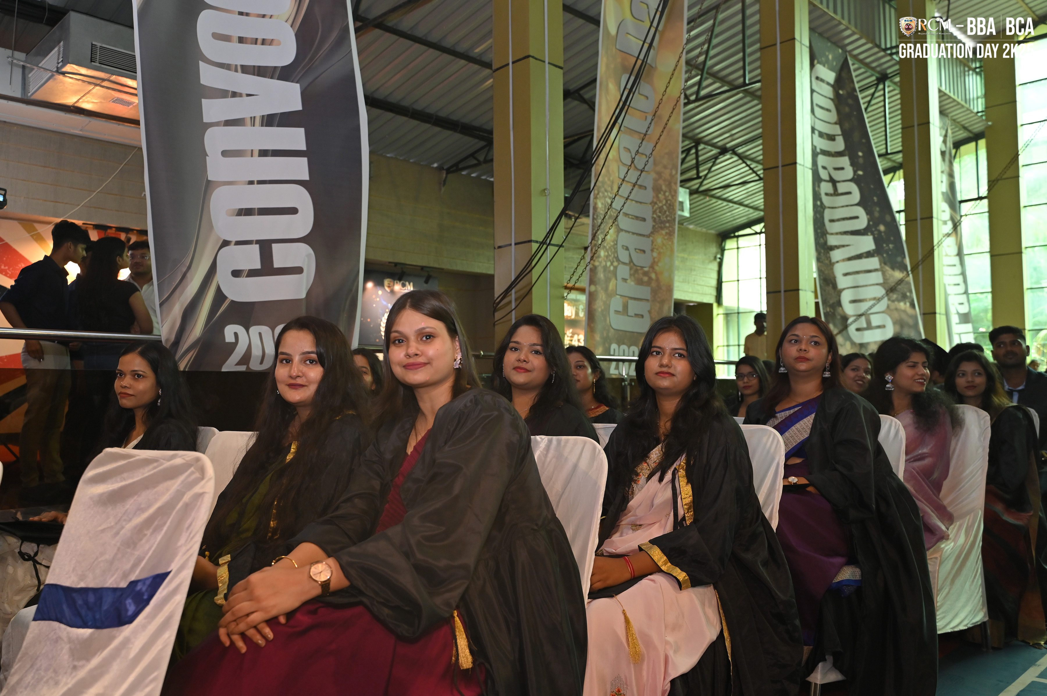 Individuals in academic gowns seated at a 2023 convocation event with celebratory banners.