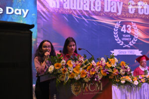 Two women at podium with flowers, speaking at Regional College of Management Graduation Day.
