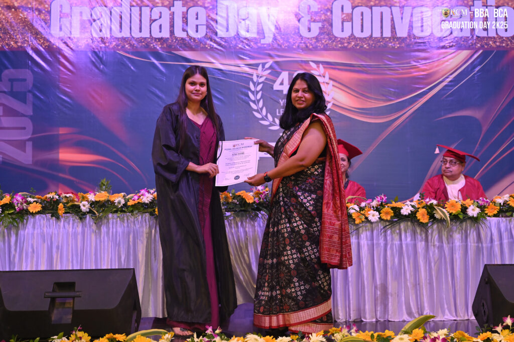 Graduate receives certificate on stage at 2023 Graduation Day, floral decor, seated officials nearby.