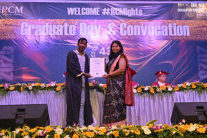 Graduation ceremony with certificate presentation on decorated stage, banner in background.