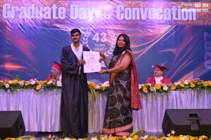 Person in graduation gown receiving certificate on stage at a decorated convocation event.