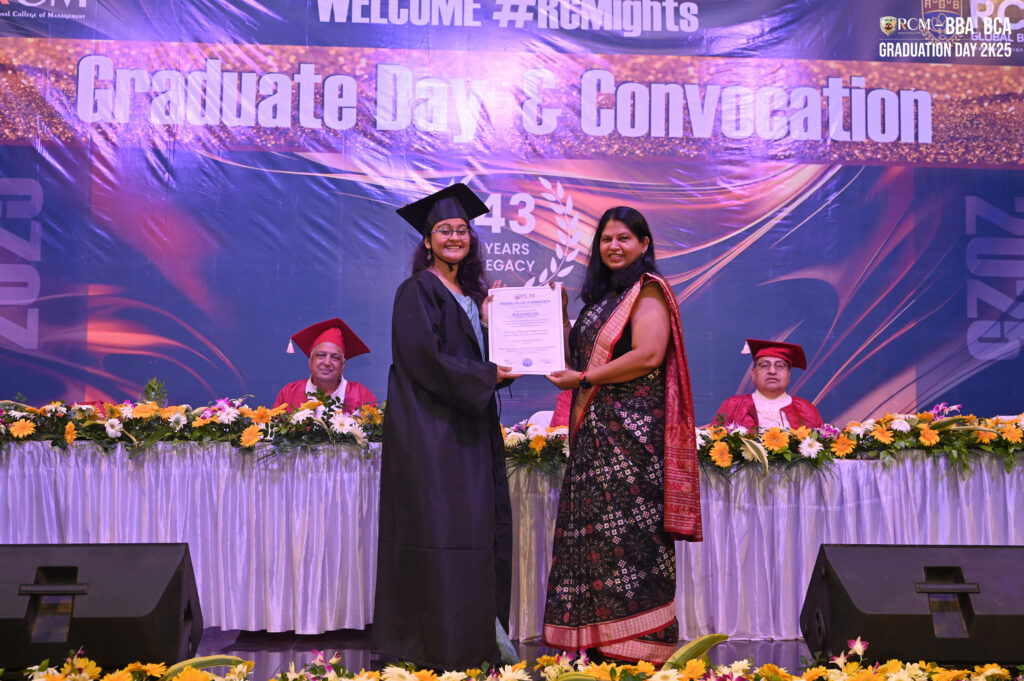 Graduate receiving a certificate on stage at a convocation ceremony with decorated banner.