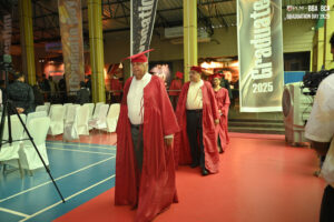 Individuals in red graduation gowns and caps walking in a 2025 graduation ceremony procession.