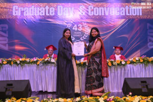 Graduation ceremony with two women on stage, banner reads "Graduate Day & Convocation."