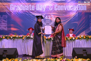 Graduate receiving a certificate on stage during a ceremony, with a banner reading "Graduate Day & Convocation."