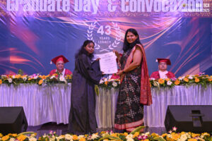 Graduate in cap and gown receives certificate on stage at convocation ceremony.