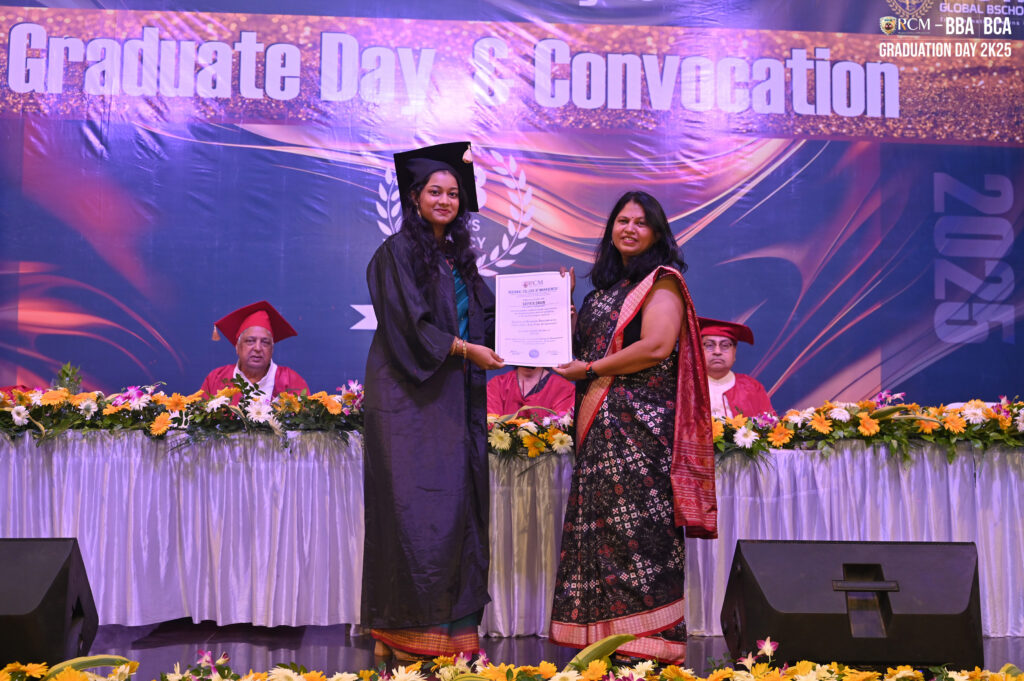 Graduate in cap and gown receiving certificate at decorated stage during ceremony.